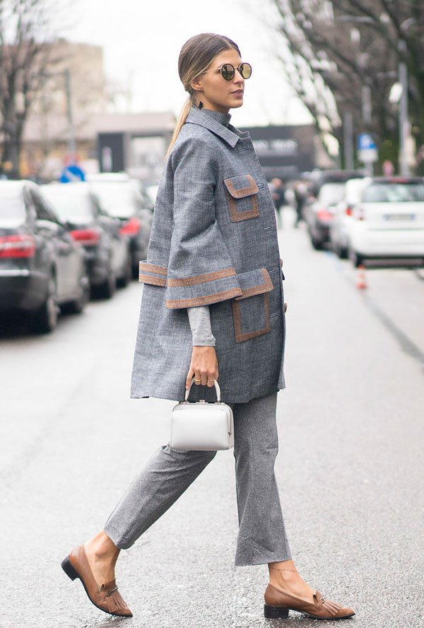Street style look Anna Fasano usando conjunto alfaiataria blazer e calça cinza, flat bege, bolsa de mão branca e óculos redondo.