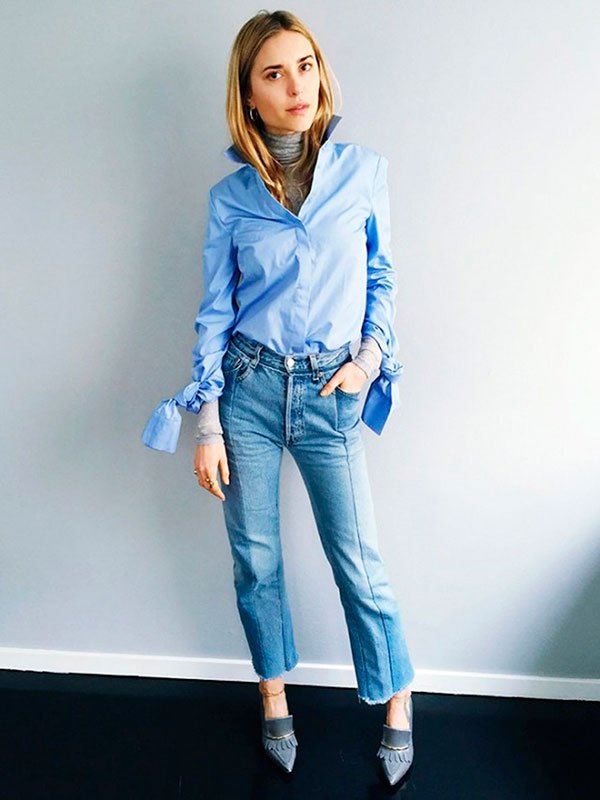 Pernille Teisbaek posa pra foto usando calça jeans de cintura alta, camisa social azul, turtleneck cinza mescla e scarpin estilo mocassim