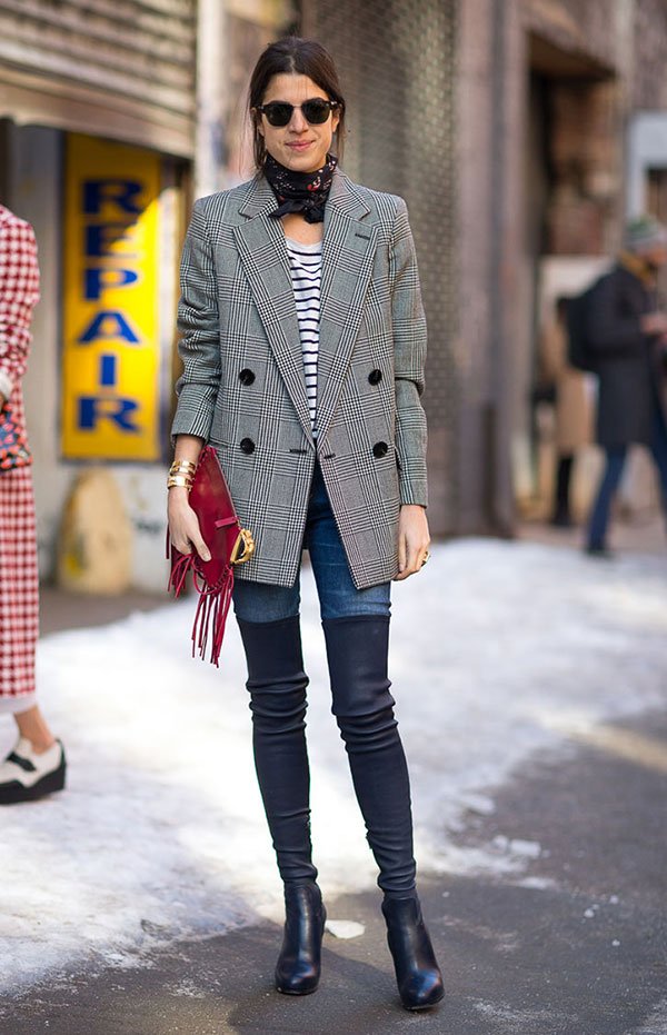 Street style look de Leandra Medine usando blazer alfaiataria xadrez, calça jeans, bota over the knee preta, lenço no pescoço e maxi clutch com franjas.