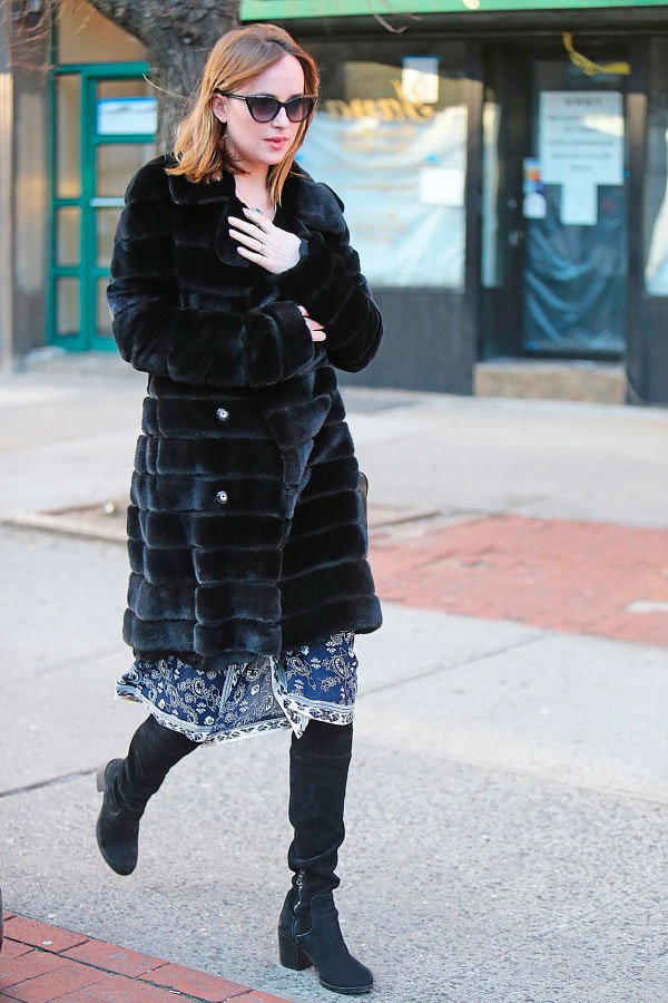 Dakota Johnson com vestido azul, casaco grande peludo e bota preta.