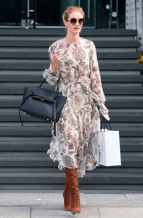 Rosie Huntington-Whiteley em street style look usando vestido longo florido, bota marrom cano alto e bolsa preta.