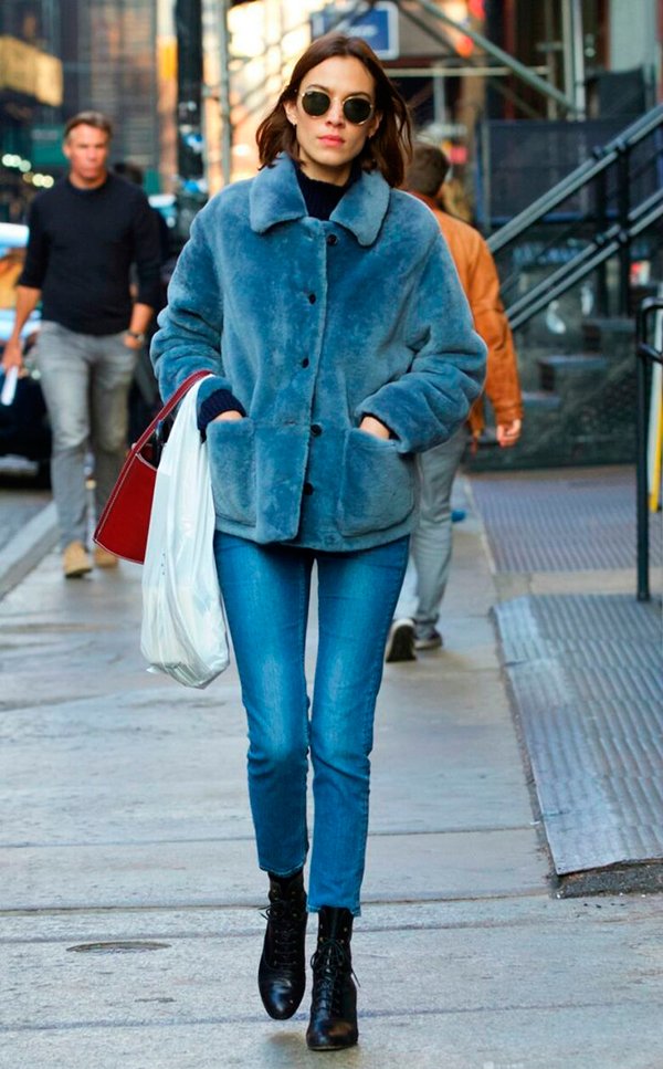 Alexa Chung posa para foto de street style usando turtleneck preta, óculos ray-ban redondo, casaco faux fur azul, calça jeans skinny azul, botas coturno preto
