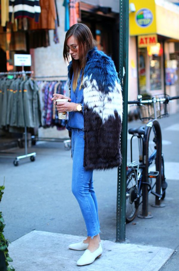 Mulher morena posa para foto de street style usando camisa jeans azul, calça skinny azul, mocassim branco, casaco faux fur em tons azuis