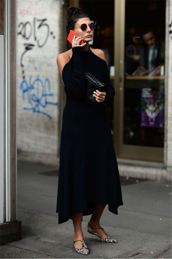 Giovanna Bataglia fala ao telefone posando para foto de street style usando vestido preto midi com ombros à mostra e sapatilha de bico fino, óculos redondo