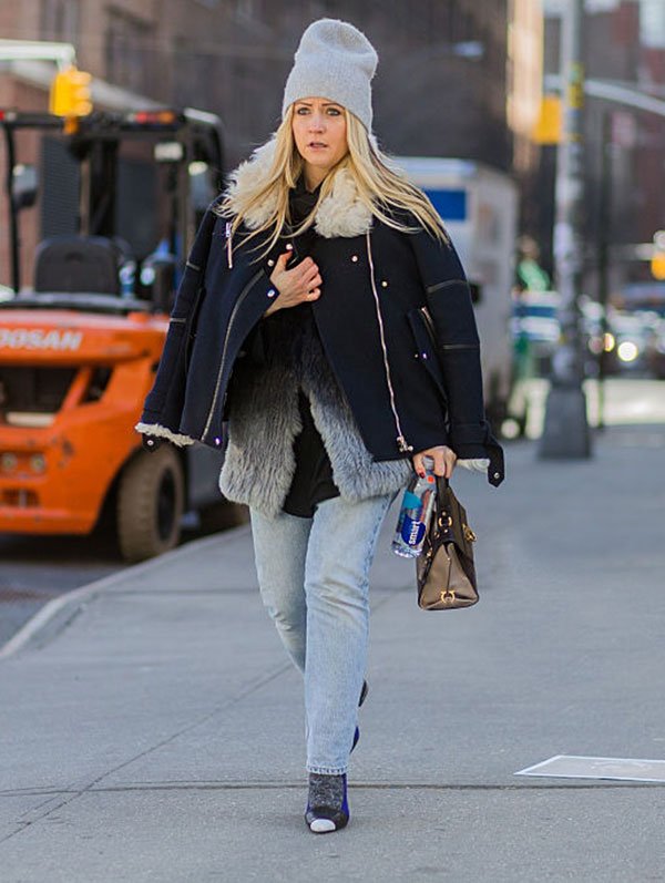 Street style look com gorro touca cinza, casaco azul, colete de pêlo fake, calça jeans e sapato salto com meia.