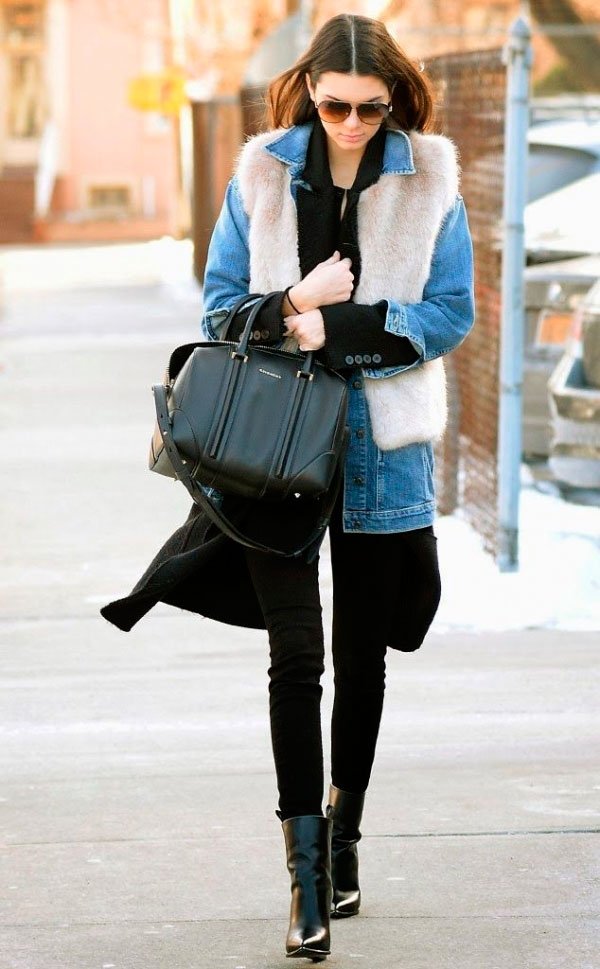 Street style look Kendall Jenner usando jaqueta jeansc, com colete de pêlo fake, calça preta e bota.
