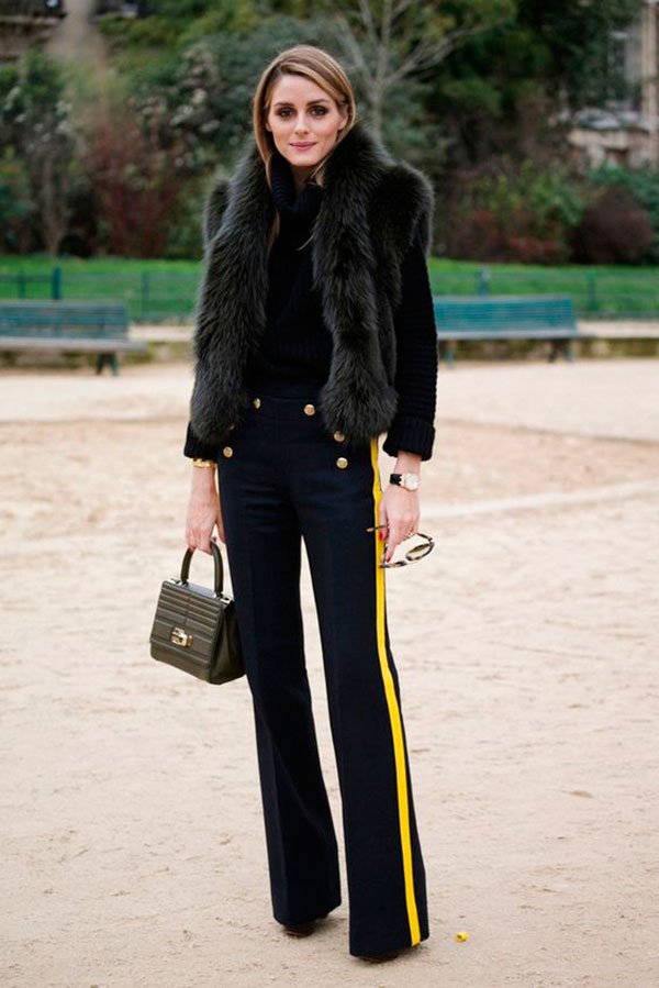 Street style look Olivia Palermo usando calça flare azul com listra amarela, blusa gola e colete de pêlo fake.