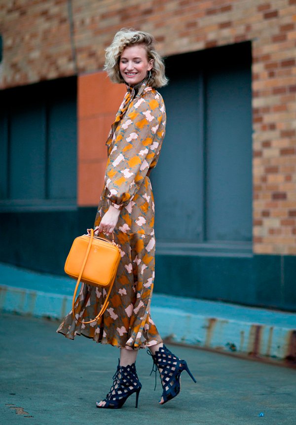 Mulher loira posa para foto de street style usando vestido com cara de pijama nude e floral, com bolsa box amarela e sandália azul marinho de amarrações