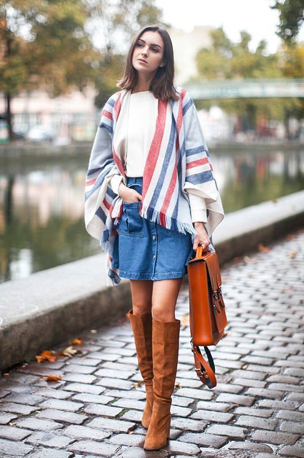Foto de street style de como usar look com t-shirt branca, saia jeans de botões, poncho de listras, botas de camurça caramelo e bolsa carteiro