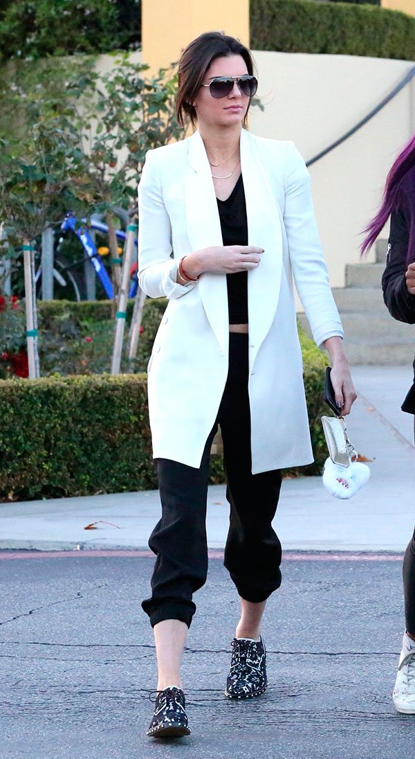 Street style look Kendall Jenner com blusa preta, calça jogging, tênis preto estampado e maxi casaco branco.