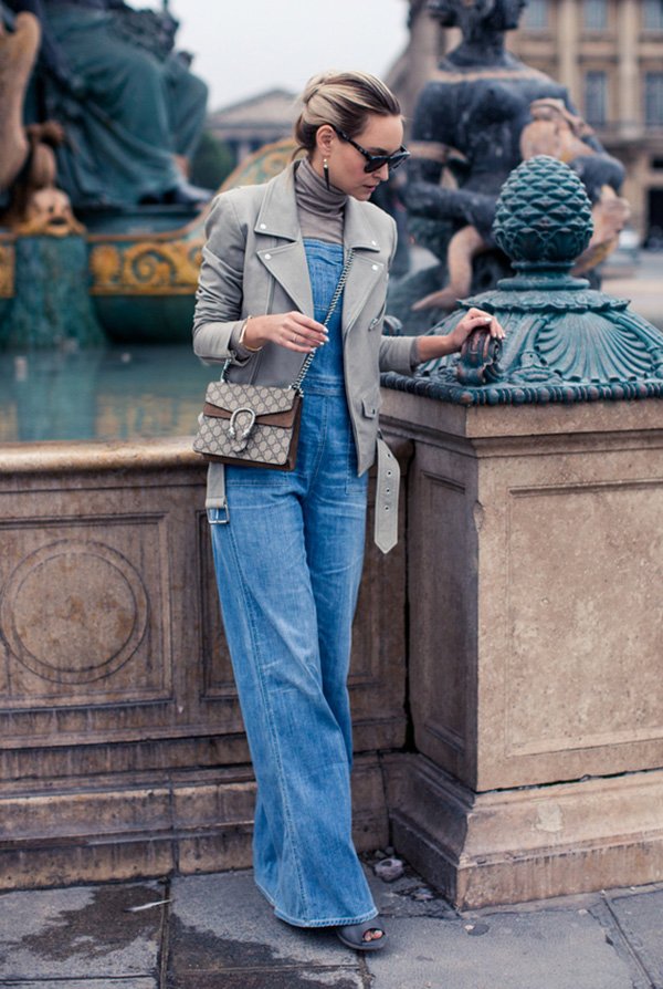 Street style look macacão jeans, turtleneck, jaqueta couro e bolsa corrente.