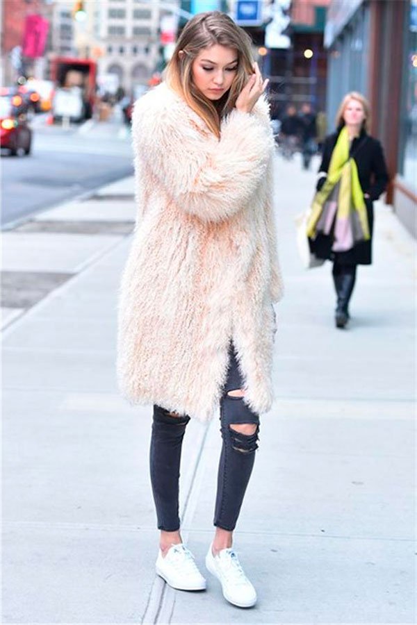 Street style look Gigi Hadid usando maxi casaco Fluffy Coat rosé, calça jeans preta rasgada e tênis branco.