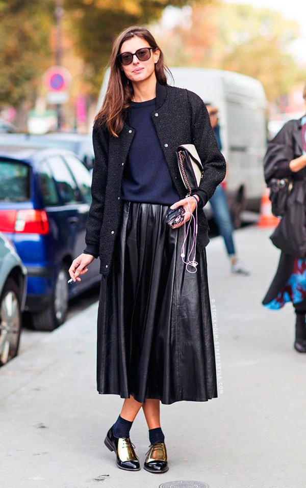 Street style look com saia midi preta, blusa azul, bomber jacket preta e sapato masculino com meia aparente.