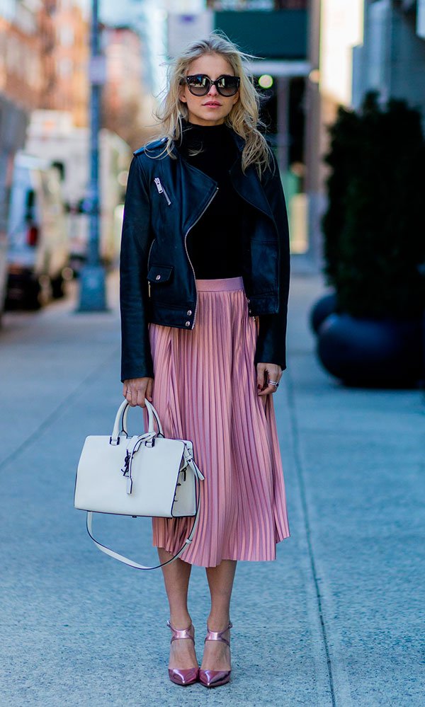 Street style look com saia plissada rosa, jaqueta de couro preta, blusa manga longa, bolsa e sapato brancos.