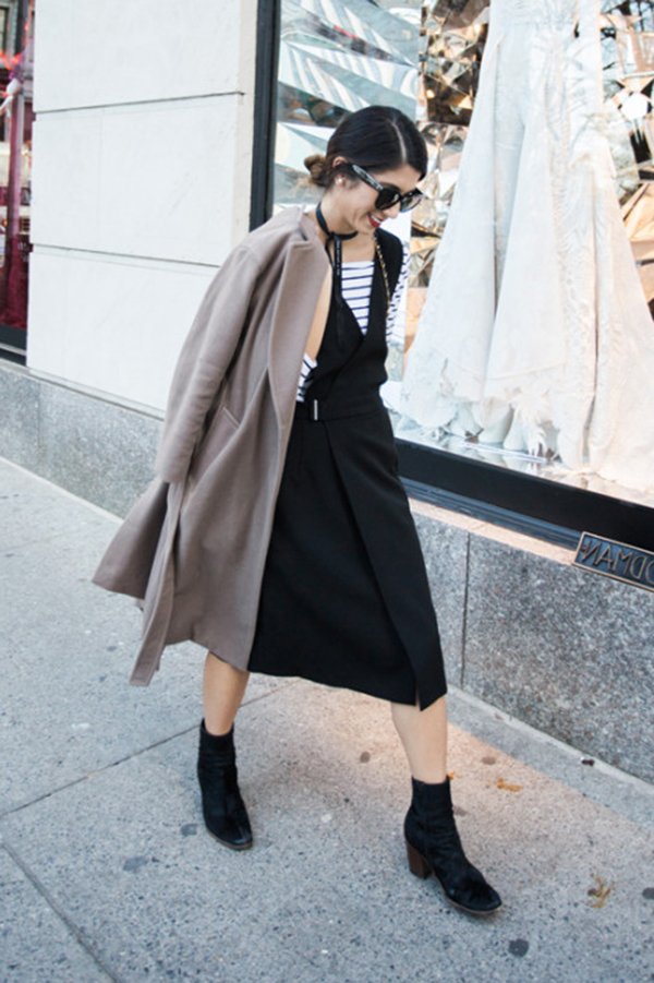 Street style look com blusa manga longa listrada, vestido decote, bota e sobretudo marrom.