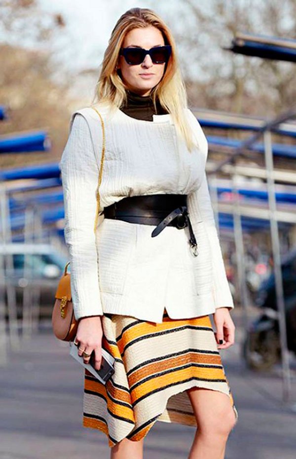 Street style look com suéter, cinto de couro e saia colorida listrada.