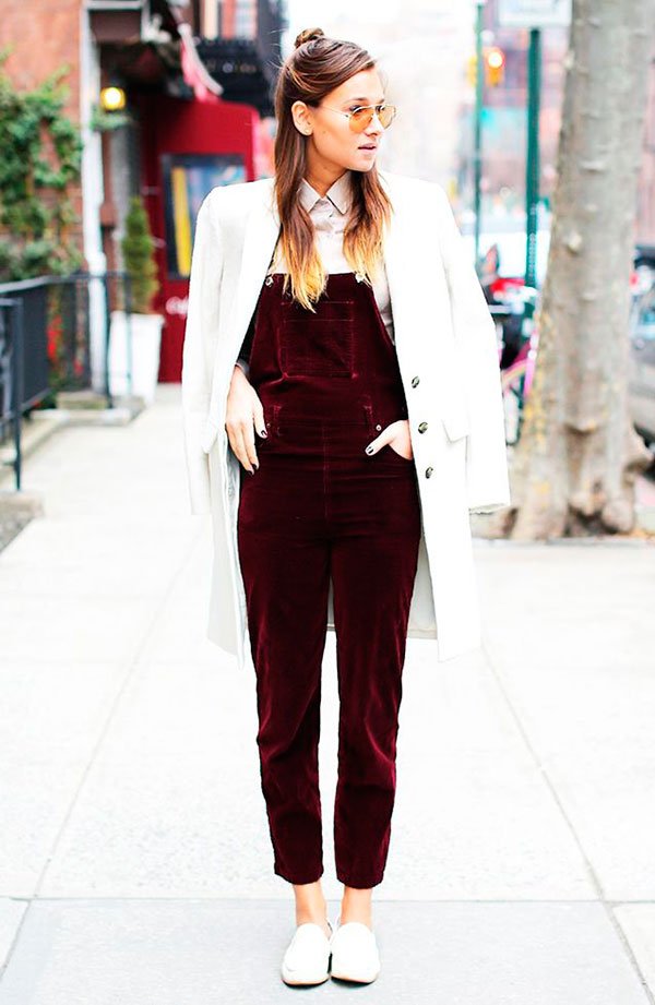 Street style look com macacão jardineira vermelho de veludo, camisa branca, sapato branco e sobretudo.