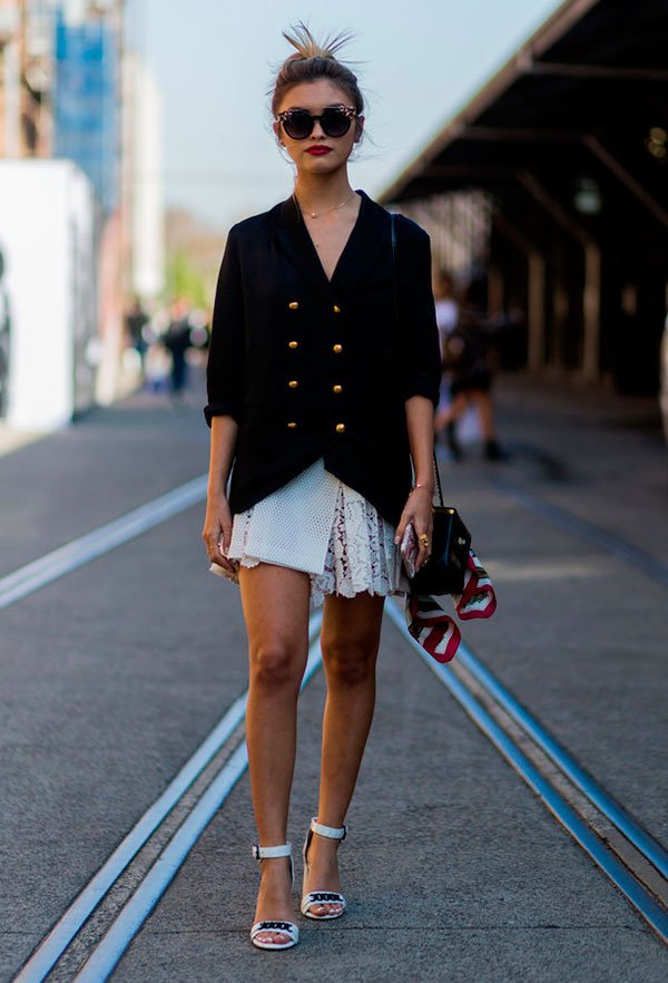 Street style look com vestido branco curto de renda com blazer oversized abotoado e sandália de salto branca.