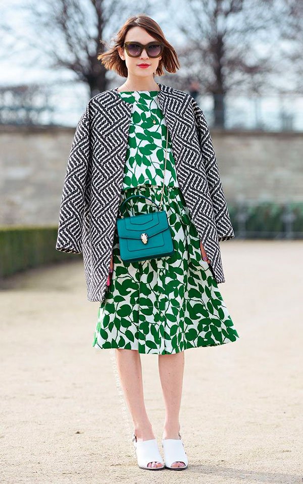 Street style look com casaco preto e branco, vestido midi verde estampado e sapato branco.