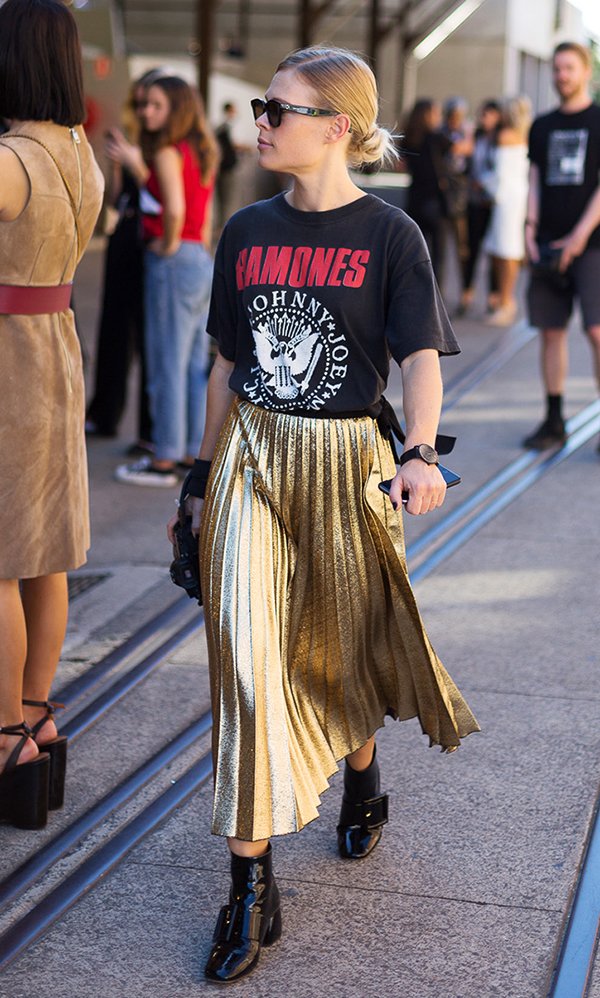 Street style de t-shirt de banda, saia plissada dourada e bota de verniz