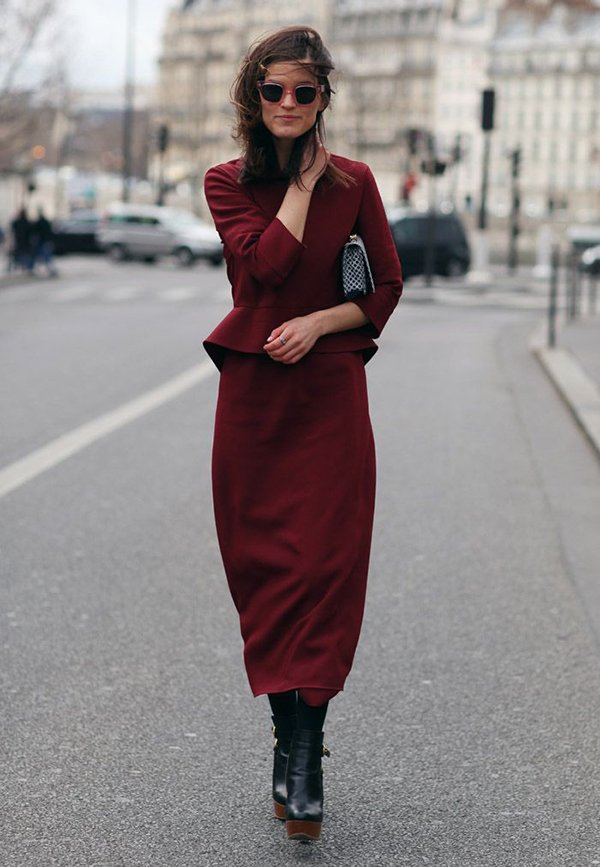 Mulher posa para foto de street style usando vestido midi burgundy, botas pretas e bolsa quadriculada