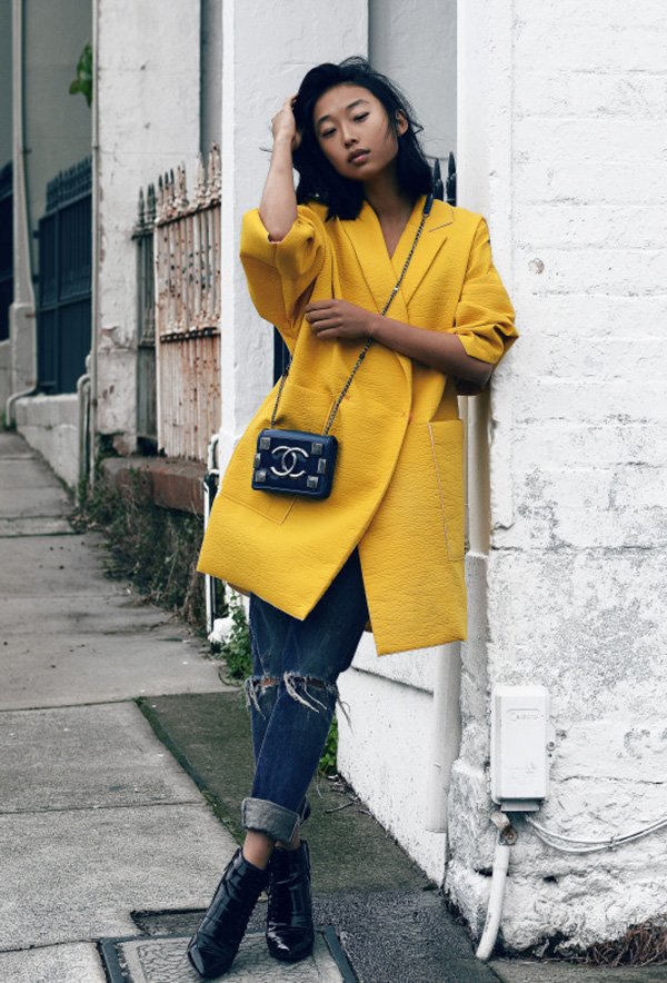 Street style look com casaco amarelo, calça jeans e bota verniz.