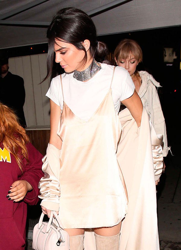 Kendall com slip dress, camiseta branca, bota OTK e choker prata.