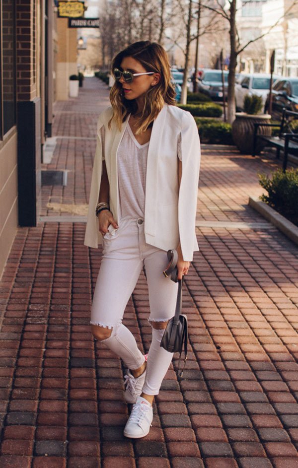 Street style look com calça branca rasgada, blazer e tênis.