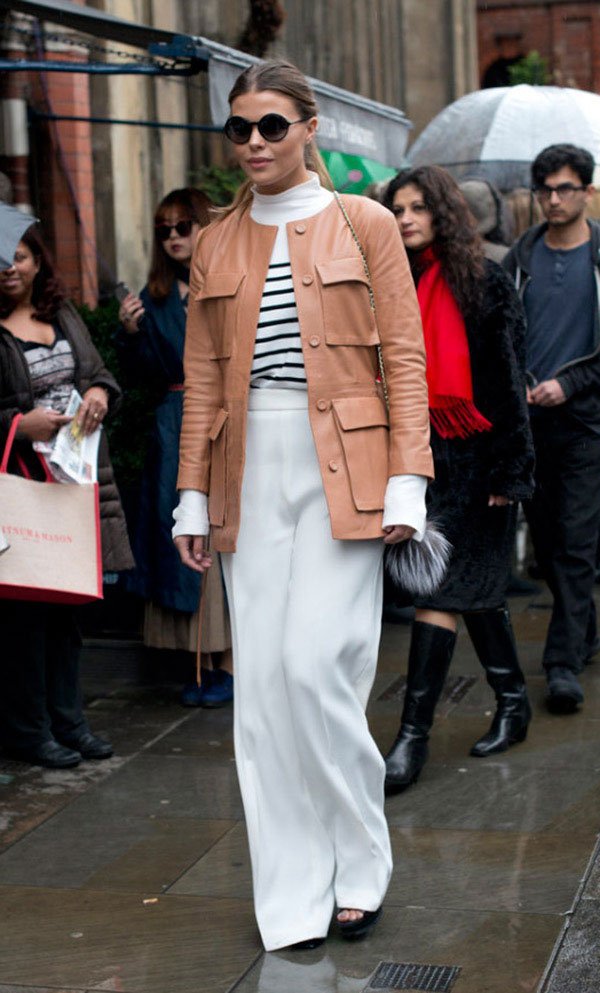 Street style look com blusa listrada, calça branca e casaco bege.