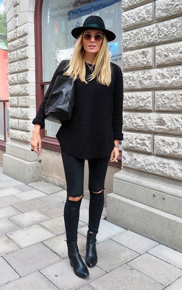 Street style look total black com chapéu, blusa calça rasgada e botas.