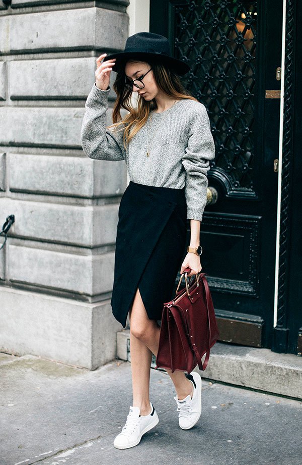 Street style look com saia social fenda, suéter cinza, tênis branco e óculos grau.