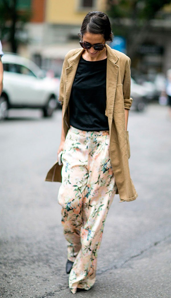 Street style look com trench coat bege, blusa preta e calça estampada.