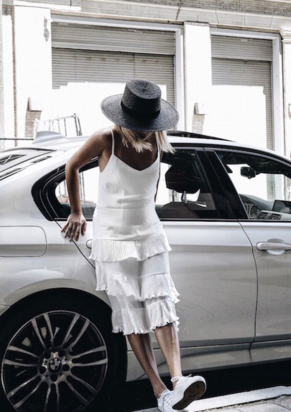 Street style look com vestido branco, chapéu e tênis.
