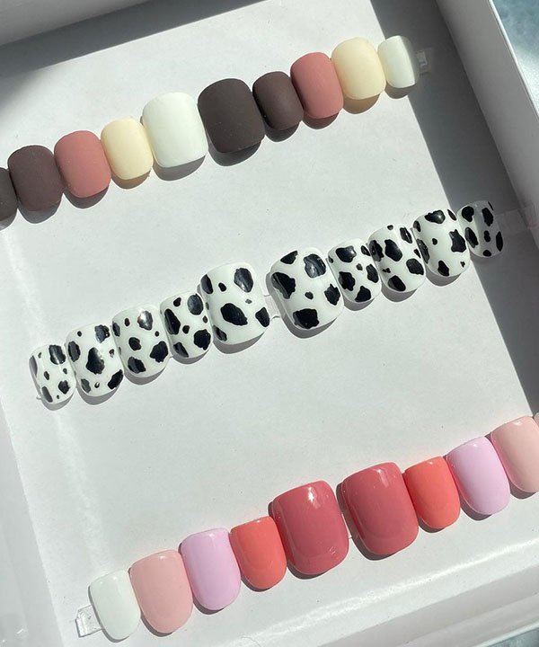 Variedade de unhas postiças decoradas, apresentando cores sólidas em tons pastéis e vibrantes, além de um estilo animal print em preto e branco. Tendência em nail art para personalizar o visual com modernidade e criatividade.