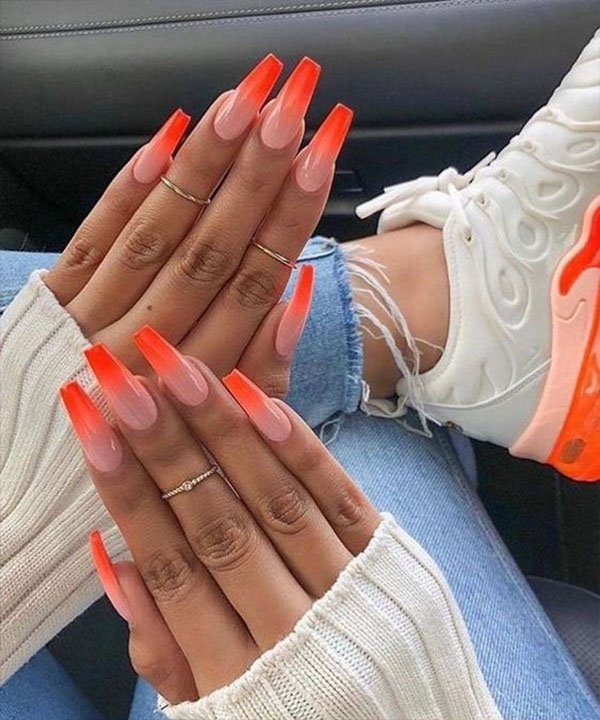 Unhas postiças stiletto com degradê laranja moderno, anéis delicados, jeans rasgados na barra, suéter branco com mangas compridas e tênis branco com solado laranja chamativo. Ideal para destacar personalidade e tendência.