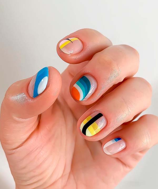 Unhas pintadas com design geométrico e cores vibrantes: amarelo, azul, laranja e preto. Tendência de nail art moderna com desenhos abstratos e padronizações coloridas, destacando criatividade e ousadia no visual. Ideal para um look estiloso e único.