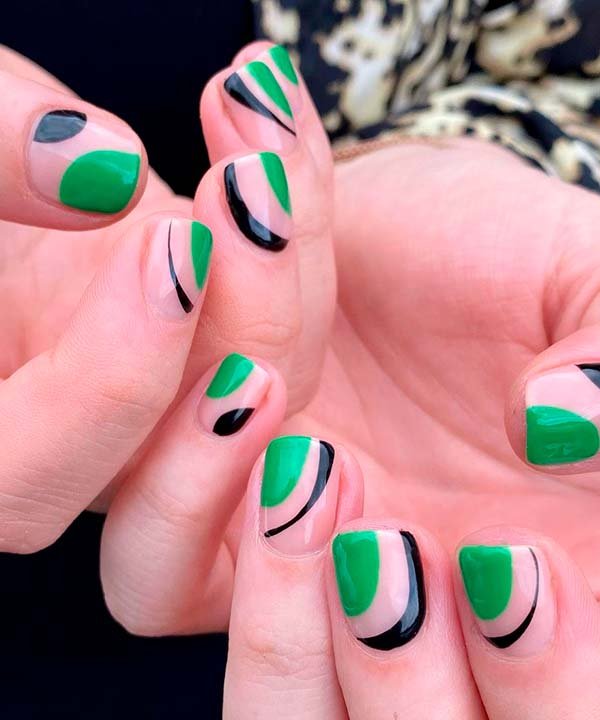 Unhas com nail art geométrica em tons de verde e preto sobre base natural. Tendência atual em decoração de unhas destacando formas abstratas e cores vibrantes, ideal para um look moderno e estiloso. Flor de estampa animal no fundo complementa o estilo.