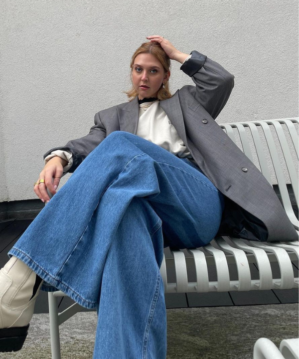 Madison Eley - camiseta e calça jeans com blazer oversized e bota - looks em dias chuvosos - Primavera - sentada em um banco branco - https://stealthelook.com.br