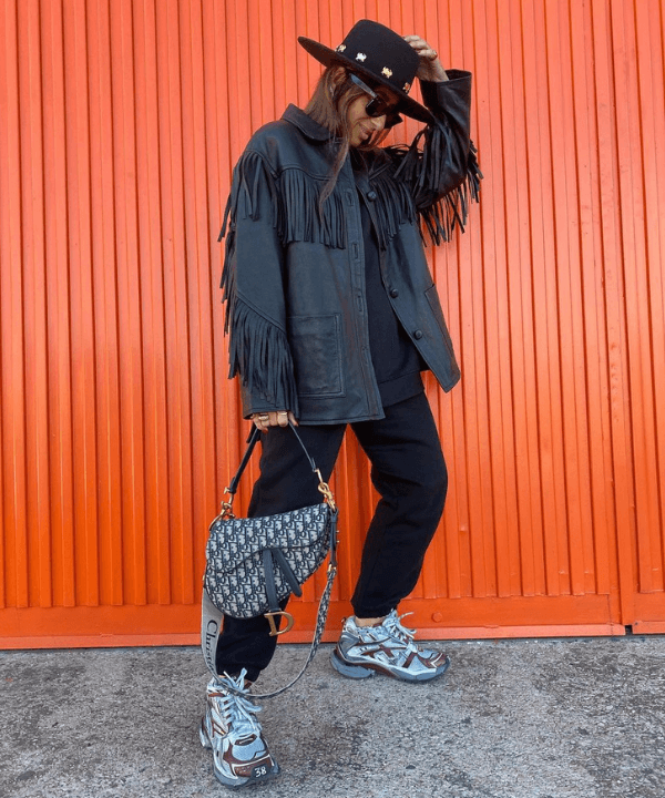 Laura Eguizabal - jaqueta de franjas preta, calça preta e chapéu - tendência dos anos 70 - Inverno - em pé na rua - https://stealthelook.com.br