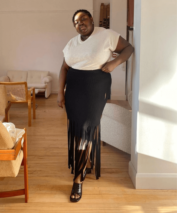 Abisola Omole - saia de franjas preta e blusa branca - tendência dos anos 70 - verão - em pé na casa  - https://stealthelook.com.br