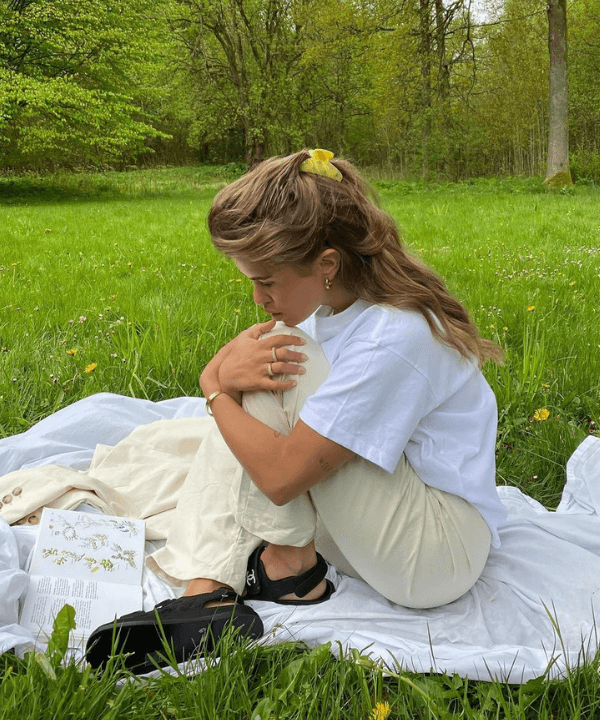 Matilda Djerf - calça bege e t-shirt branca - cottagecore - verão - sentada em um campo - https://stealthelook.com.br