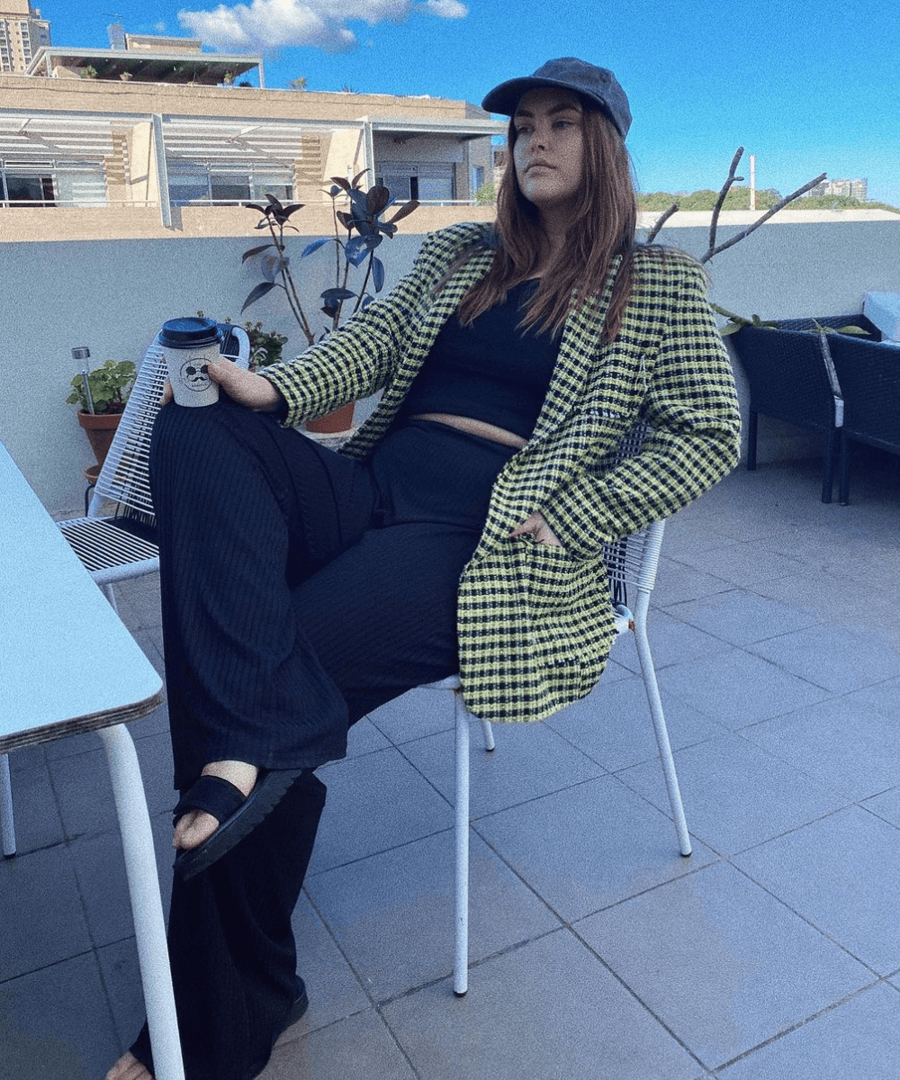 Sophia Brenn - top e calça preta com blazer xadrez e boné - looks com chapéu - Verão 2022 - sentada na cadeira - https://stealthelook.com.br