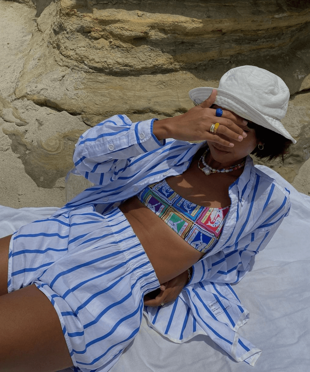 Stephanie Arant - conjunto listrado de shorts e camisa, bucket hat e acessórios de miçanga - moda praia - verão - deitada na praia - https://stealthelook.com.br