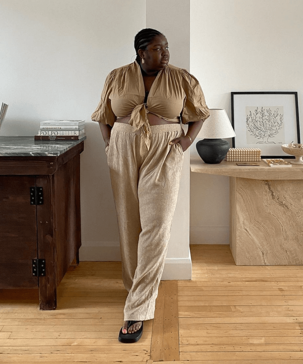 Abisola Omole - calça bege e camisa marrom - looks de verão - verão - em pé na casa  - https://stealthelook.com.br