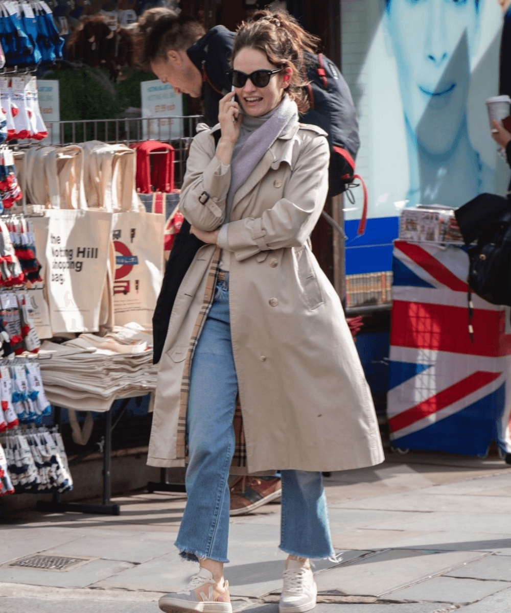 Lily James - calça jeans, trench coat e tênis - Lily James - Inverno  - andando na rua - https://stealthelook.com.br