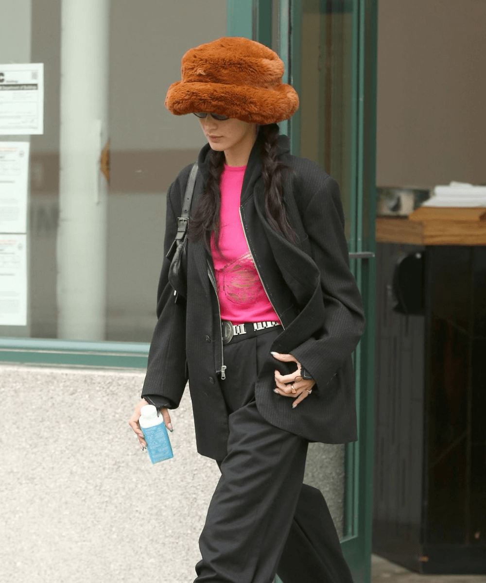 Bella Hadid - calça preta, blusa rosa e bucket hat de pelúcia marrom - tendência de inverno - Inverno  - andando na rua - https://stealthelook.com.br