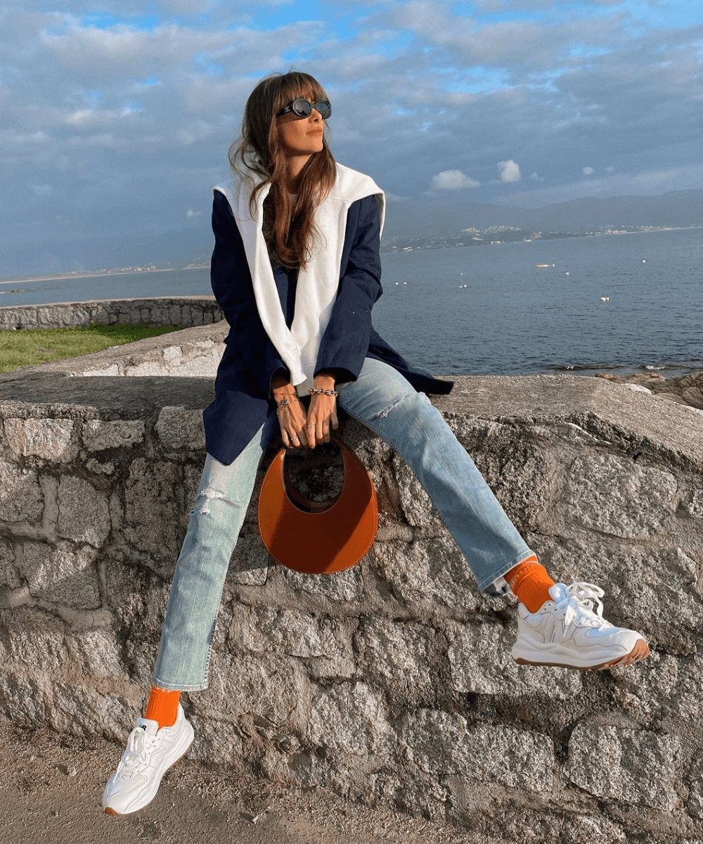 Julie Sergent Ferreri - calça jeans, meias laranjas, tênis e trico azul - looks novos - Outono - sentada em uma mureta com as duas pernas esticadas e abertas - https://stealthelook.com.br