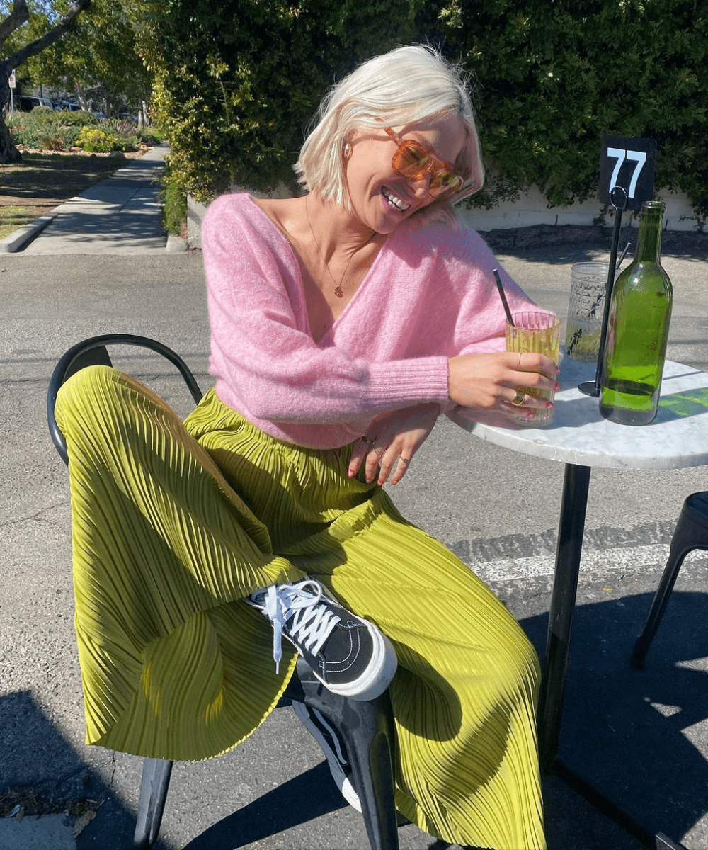 Martha | @marthaeelman - calça verde plissada, tênis vans e tricot rosa - looks novos - Outono - sentada em uma cadeira com as duas pernas flexionadas, tomando um suco - https://stealthelook.com.br