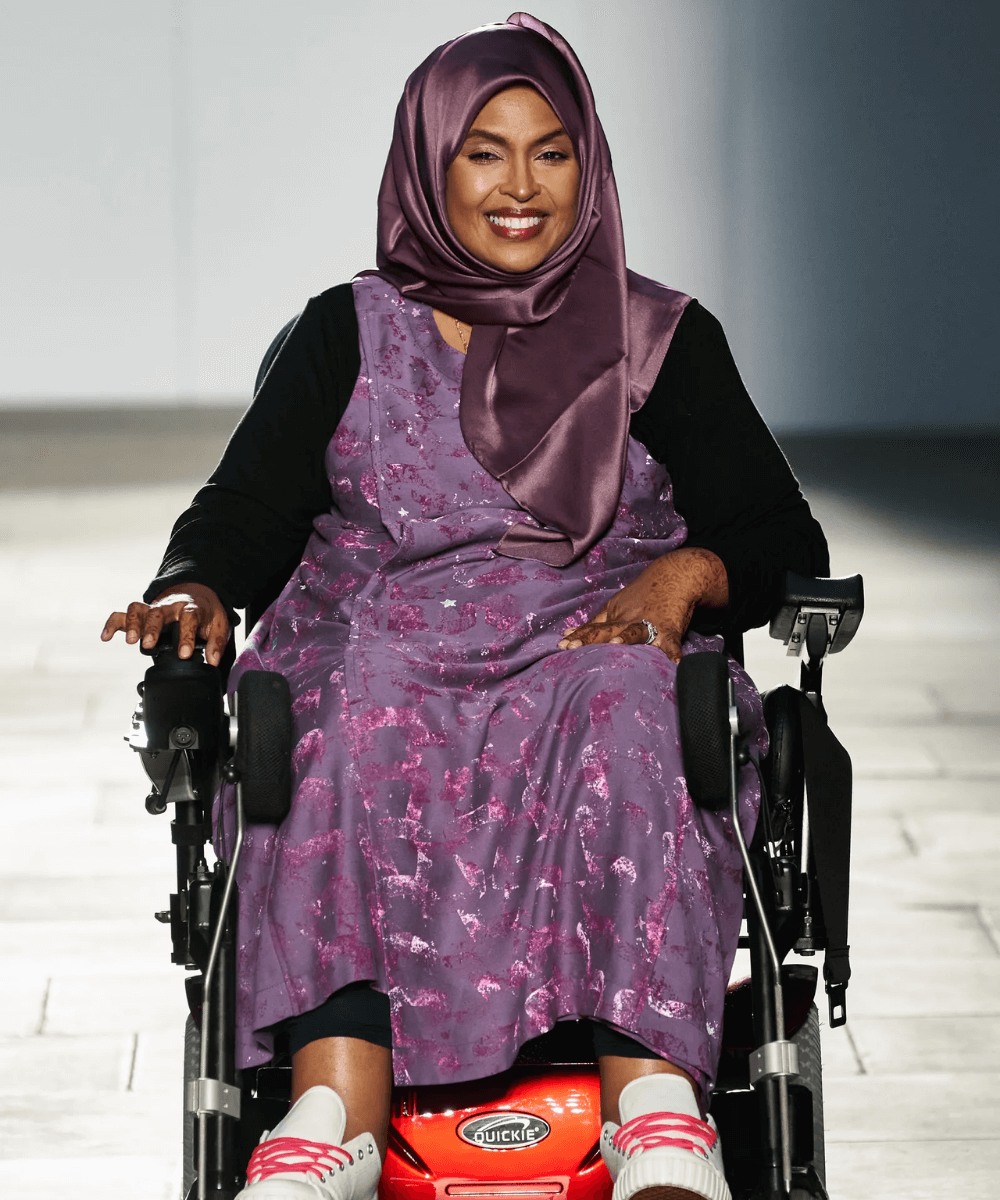 Faduma Farah - vestido roxo e blusa de manga longa preta - diversidade nas passarelas - Inverno  - em uma cadeira de rodas na passarela - https://stealthelook.com.br