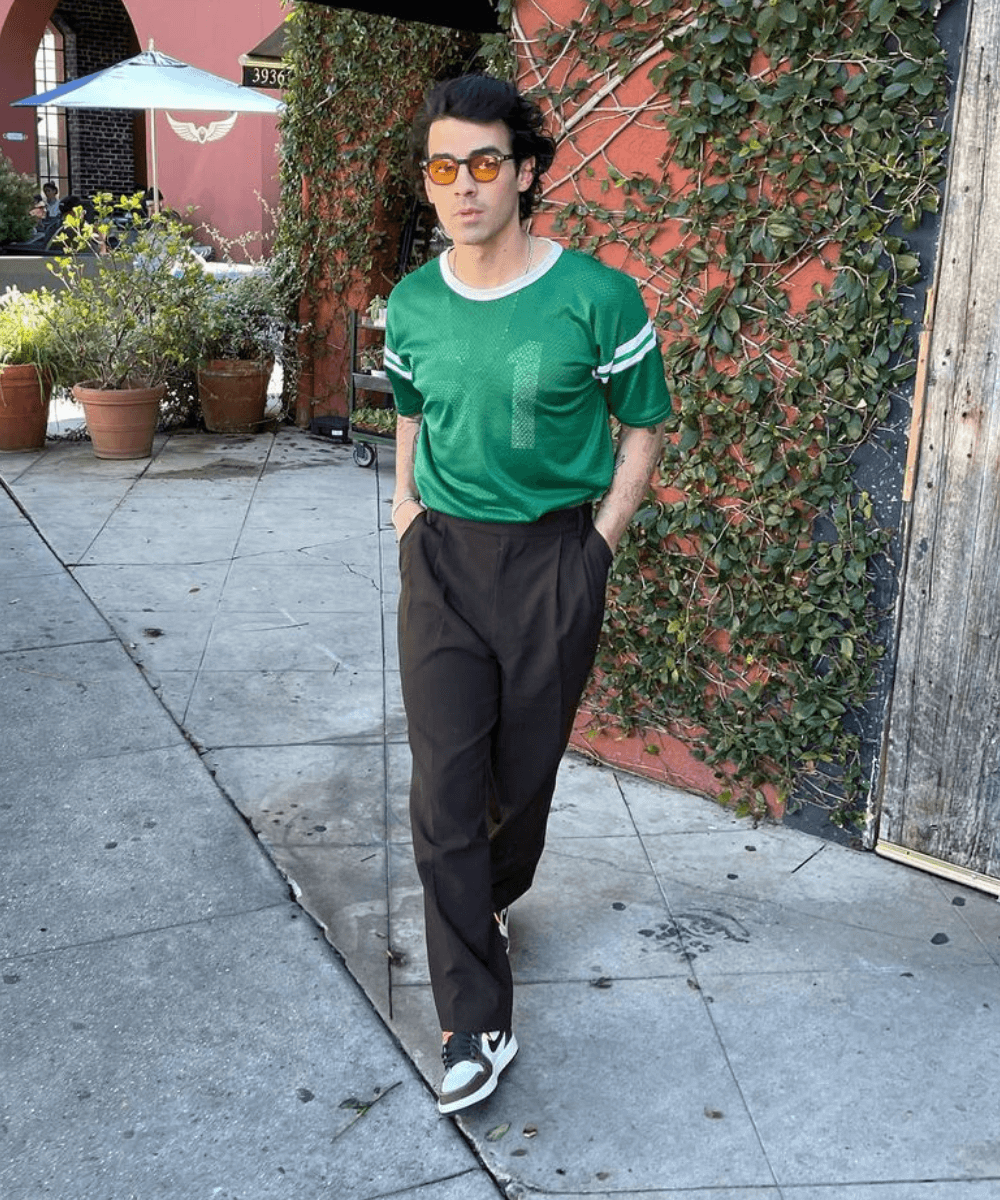 Joe Jonas - calça preta, blusa verde e tênis - Joe Jonas - Primavera - em pé na rua com as pernas cruzadas - https://stealthelook.com.br